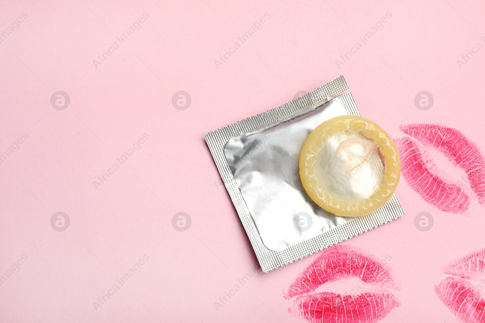 Photo of Condom with lipstick kiss marks and space for text on pink background, flat lay. Safe sex