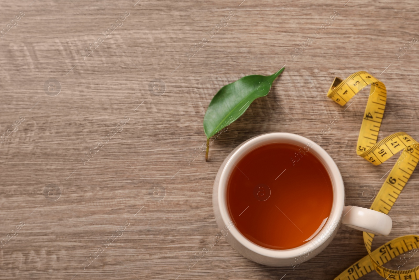 Photo of Cup of herbal diet tea and measuring tape on wooden table, flat lay with space for text. Weight loss concept