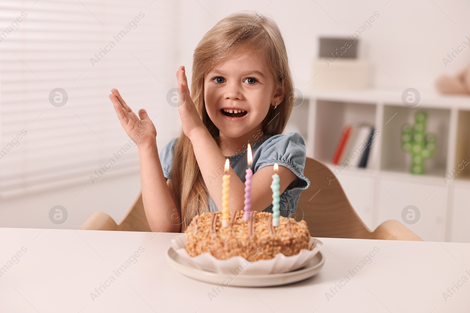 Photo of Cute girl with birthday cake at table indoors