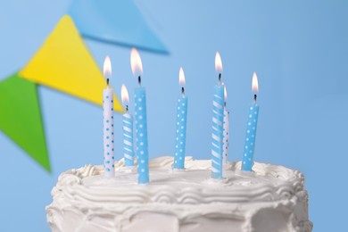 Delicious cake with burning candles and festive decor on light blue background, closeup