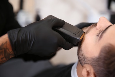 Professional hairdresser shaving client with electric razor in barbershop