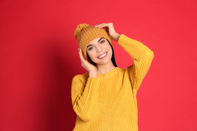 Photo of Young woman wearing warm sweater and hat on red background. Winter season
