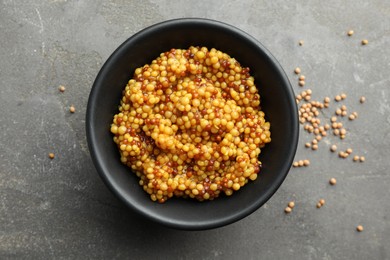 Photo of Whole grain mustard in bowl and dry seeds on grey table, flat lay