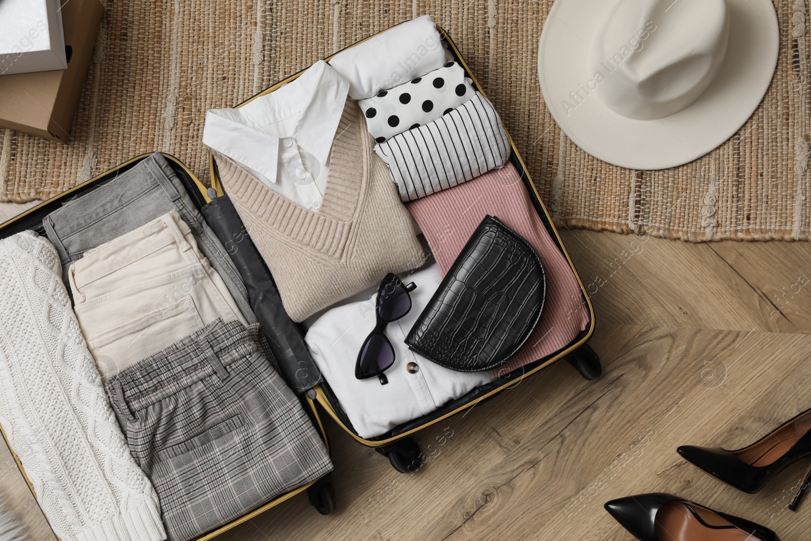 Photo of Open suitcase with folded clothes, accessories and shoes on floor, flat lay