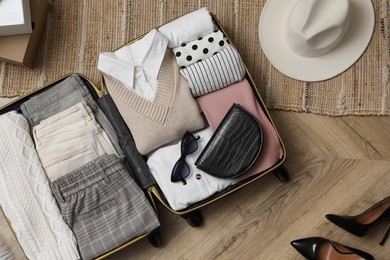 Open suitcase with folded clothes, accessories and shoes on floor, flat lay