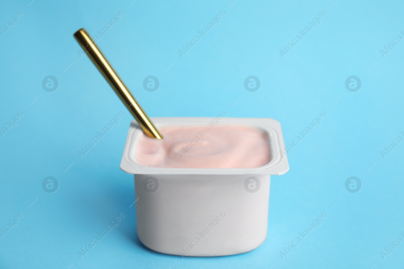 Photo of Tasty organic yogurt with spoon on light blue background