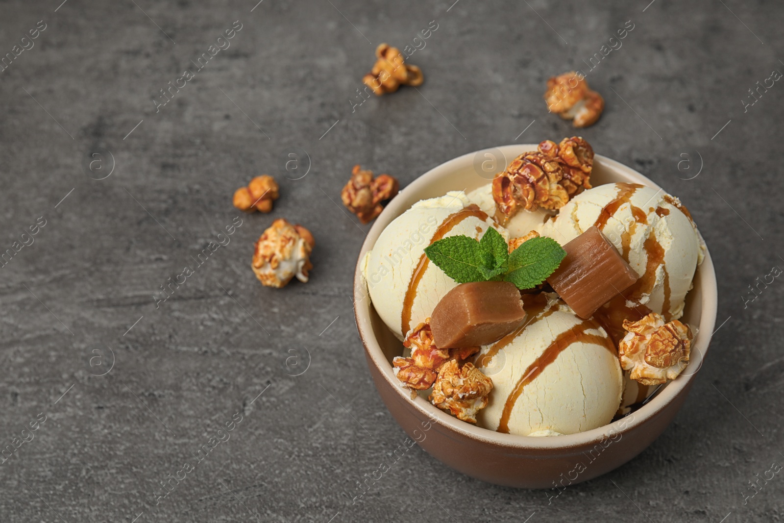 Photo of Delicious ice cream with caramel and popcorn in bowl on table. Space for text
