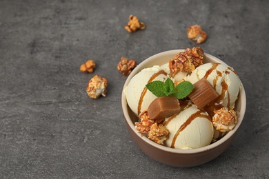 Delicious ice cream with caramel and popcorn in bowl on table. Space for text