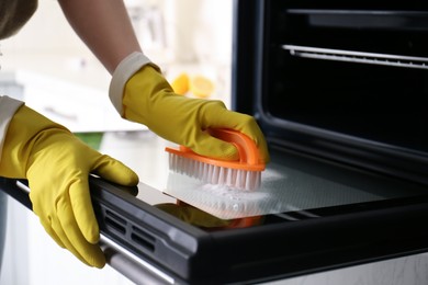 Photo of Woman cleaning oven door with baking soda in kitchen, closeup