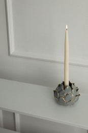 Holder with burning candle on table near white wall indoors, space for text