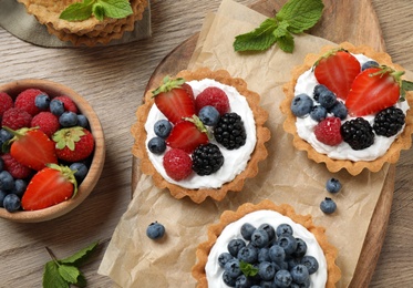 Photo of Different berry tarts on wooden table, flat lay. Delicious pastries