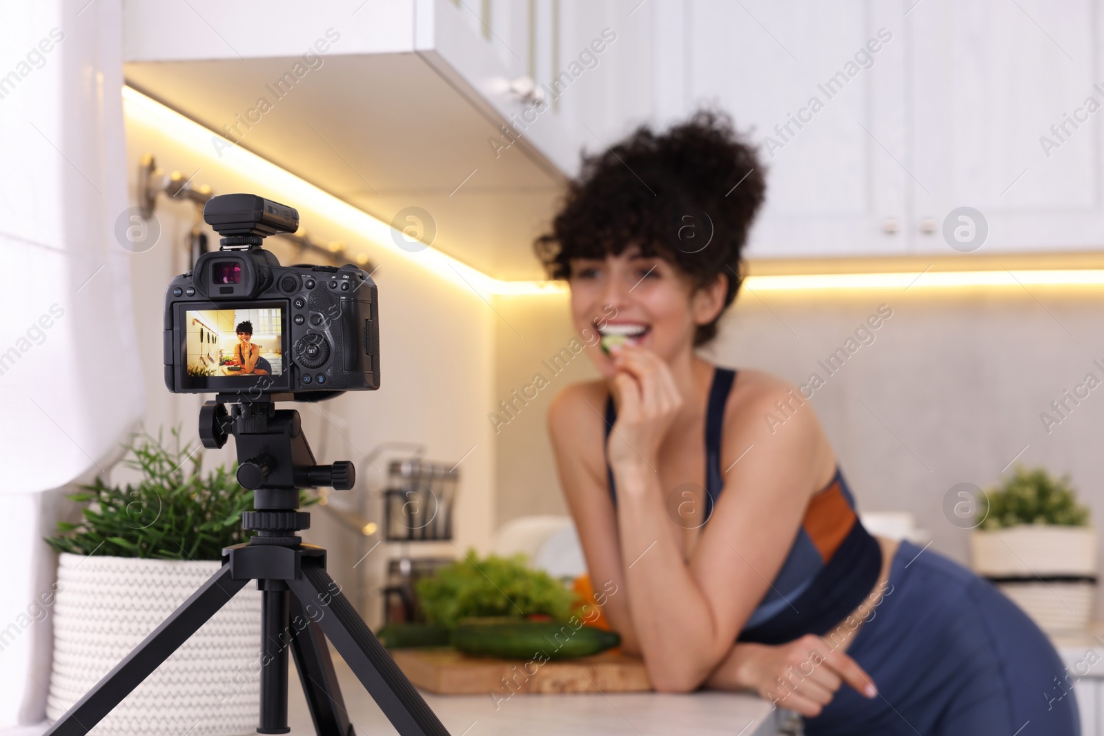 Photo of Food blogger recording video in kitchen, focus on camera