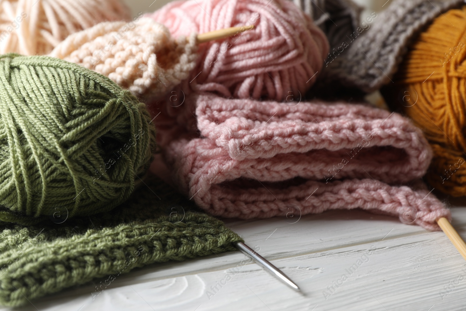 Photo of Balls of soft yarns, knitting and needles on white wooden table, closeup