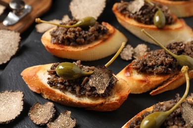 Photo of Tasty bruschettas with truffle paste and capers on black table, closeup