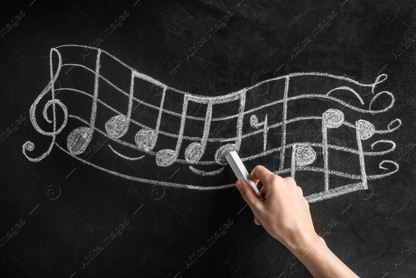 Photo of Woman writing music notes with chalk on blackboard, closeup