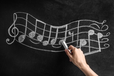 Photo of Woman writing music notes with chalk on blackboard, closeup