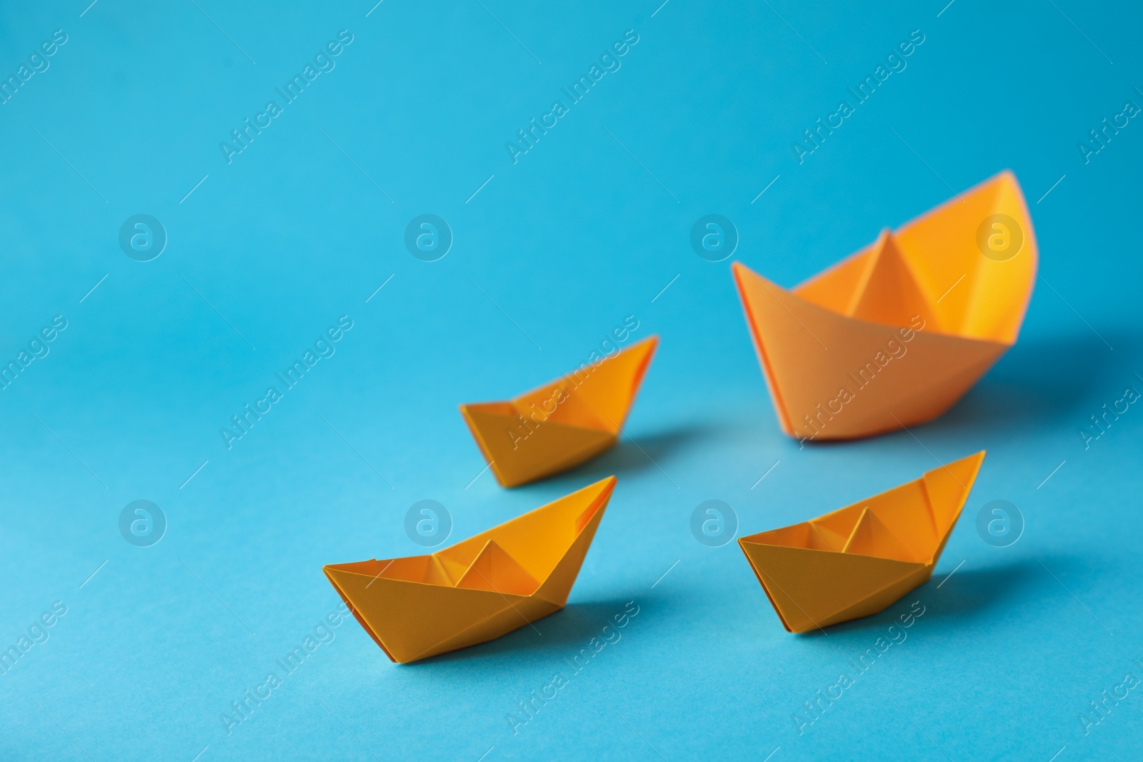 Photo of Handmade orange paper boats on light blue background. Space for text