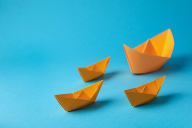 Handmade orange paper boats on light blue background. Space for text