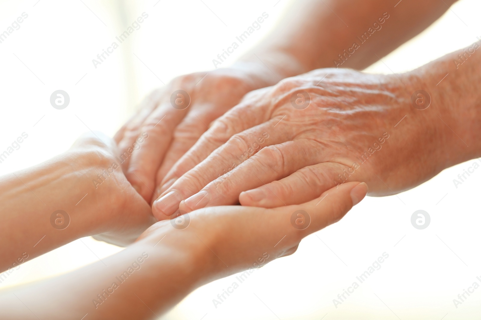 Photo of Young woman holding elderly man hands on blurred background, closeup. Help service