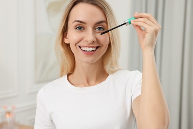 Beautiful woman applying mascara with brush indoors