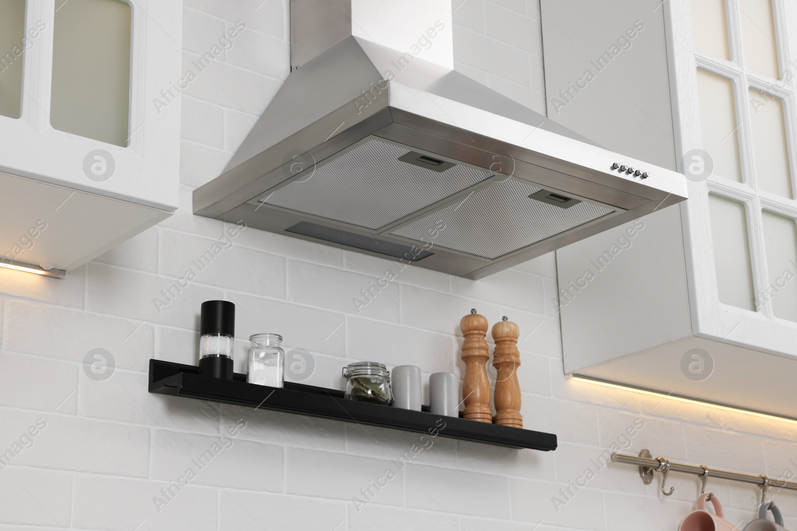 Photo of Modern range hood over shelf with spices in kitchen