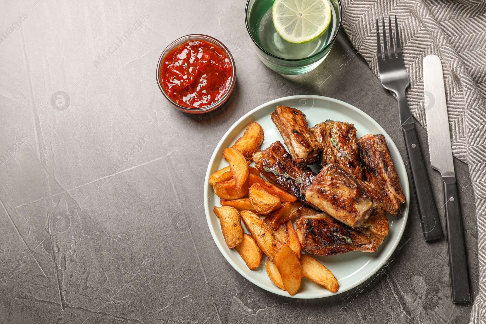 Photo of Delicious grilled ribs served on grey table, flat lay. Space for text