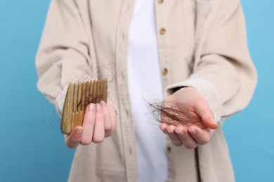 Photo of Woman holding comb with lost hair on light blue background, closeup. Alopecia problem