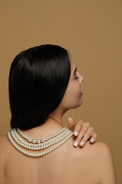 Photo of Young woman wearing elegant pearl necklace on brown background, back view