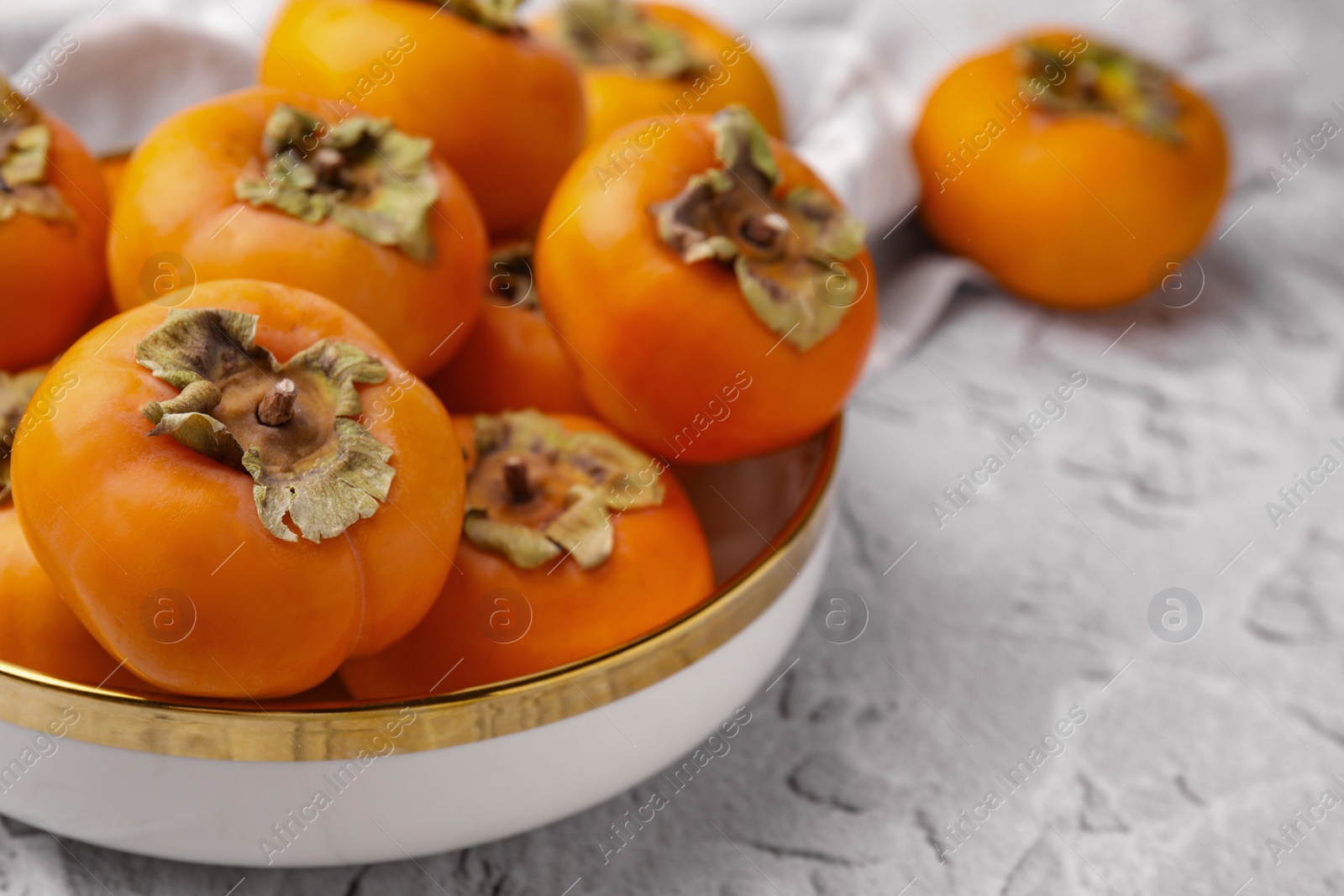 Photo of Bowl with delicious ripe juicy persimmons on white textured table, closeup. Space for text