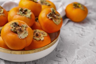 Photo of Bowl with delicious ripe juicy persimmons on white textured table, closeup. Space for text