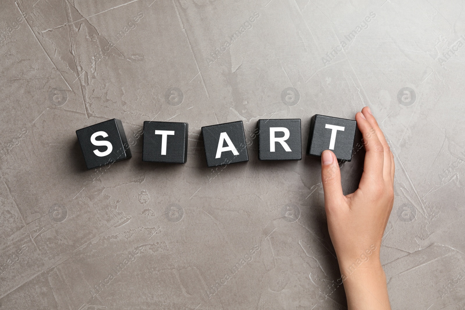 Photo of Woman making word START with black cubes on beige stone background, top view