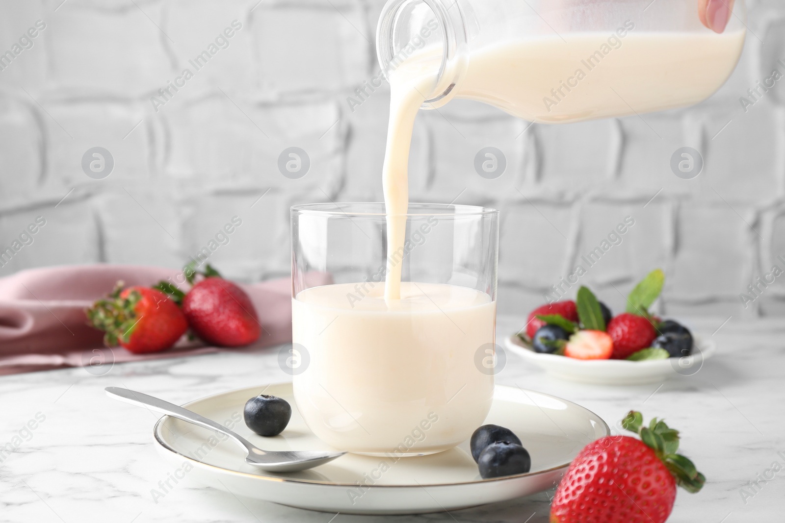 Photo of Woman pouring tasty yogurt into glass at white marble table, closeup