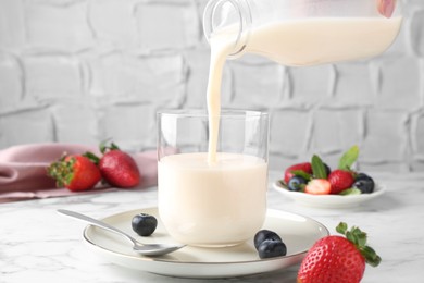 Woman pouring tasty yogurt into glass at white marble table, closeup