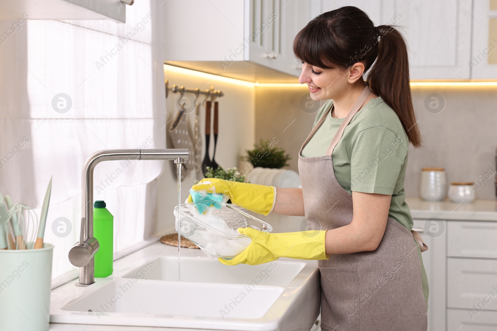 Photo of Happy young housewife washing dishes in kitchen sink. Cleaning chores