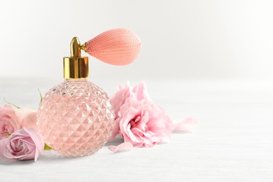 Photo of Vintage bottle of perfume and flowers on light background, space for text