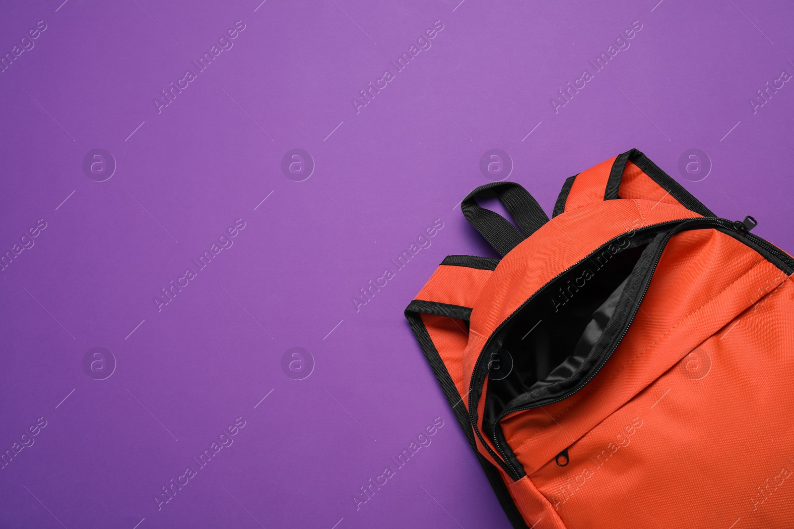 Photo of Stylish orange backpack on purple background, top view. Space for text