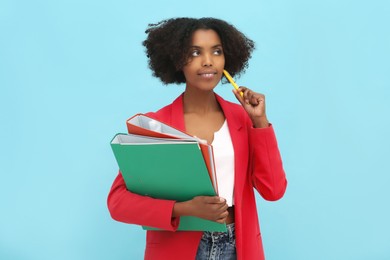 African American intern with folders and pen on light blue background