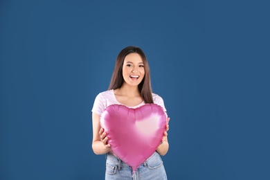 Portrait of young woman with heart shaped balloon on color background