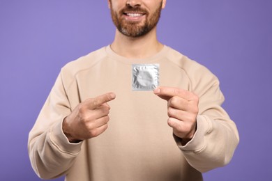 Photo of Man holding condom on purple background, closeup. Safe sex