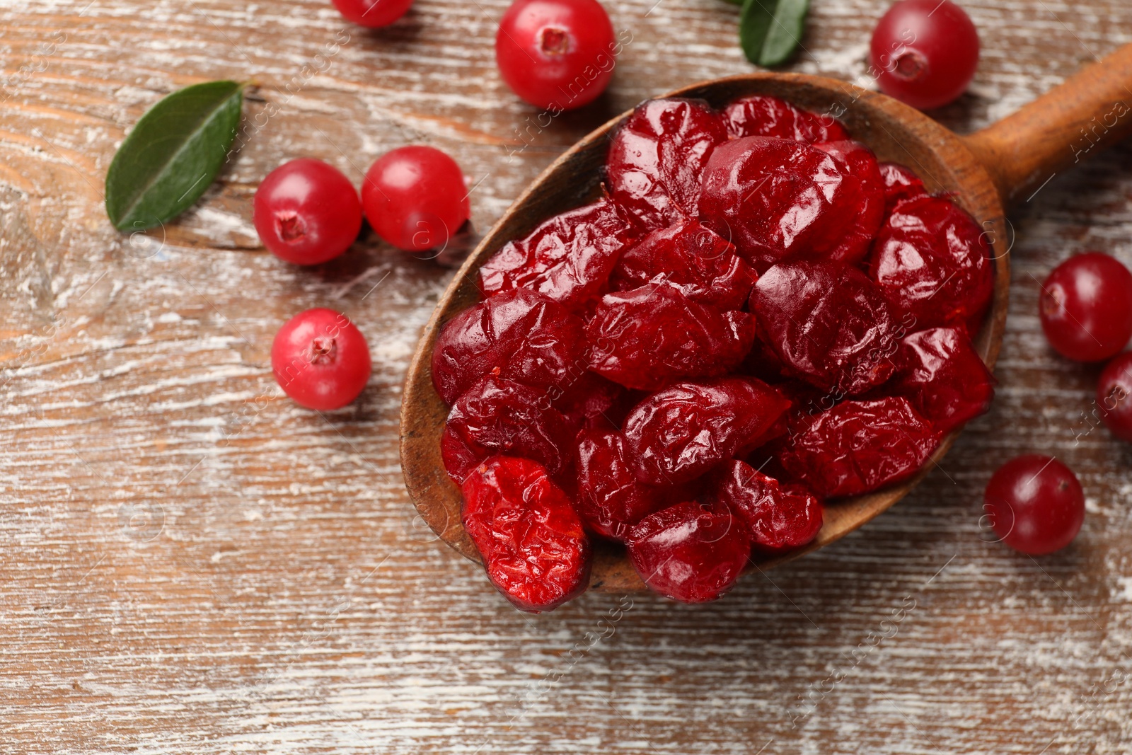 Photo of Tasty dried cranberries in spoon and fresh ones on rustic wooden table, top view