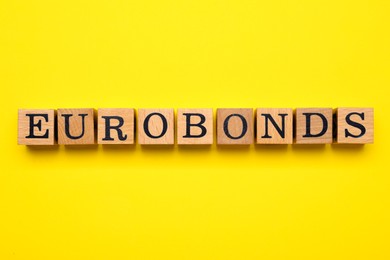 Photo of Word Eurobonds made of wooden cubes with letters on yellow background, flat lay