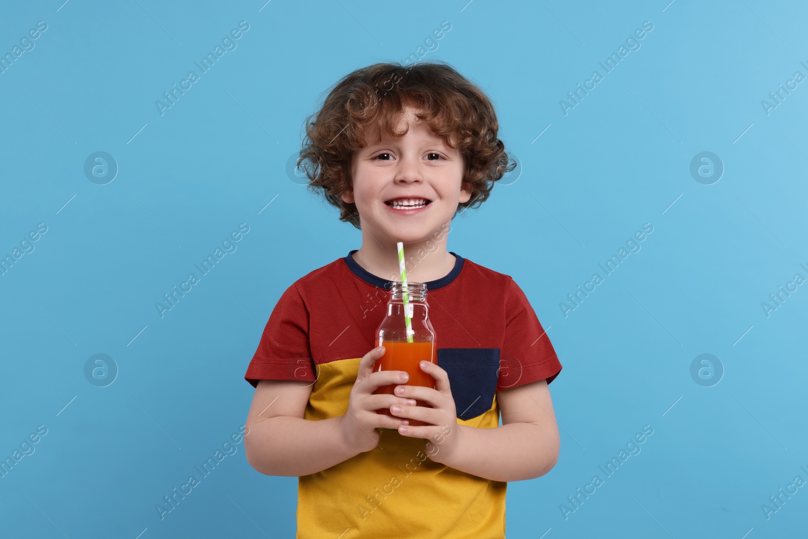 Photo of Cute little boy with glass bottle of fresh juice on light blue background