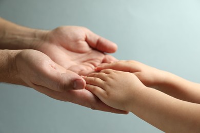 Father and child holding hands on light blue background, closeup