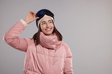 Winter sports. Happy woman with snowboard goggles on grey background, space for text