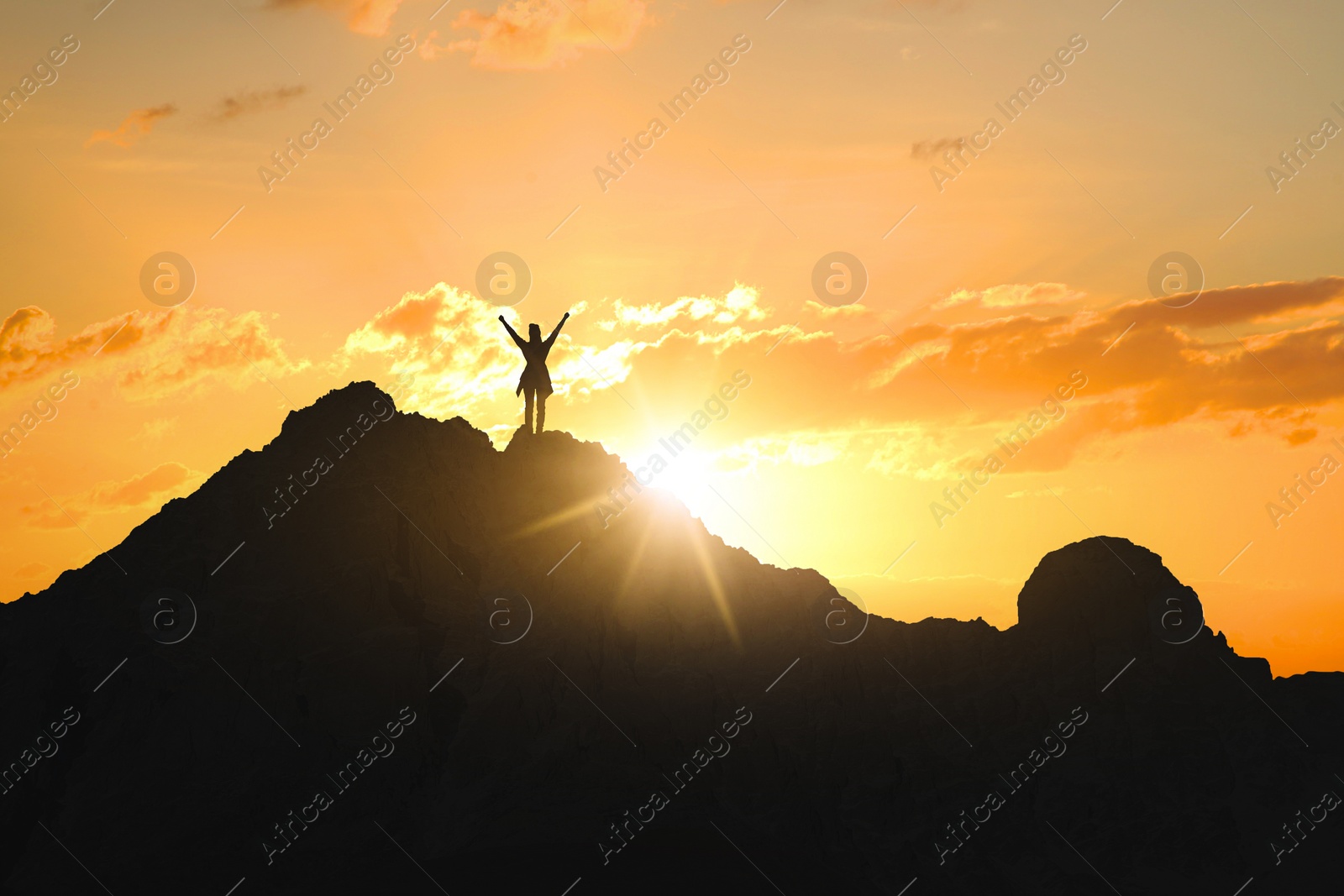 Image of Silhouette of woman in mountains under beautiful sky at sunset