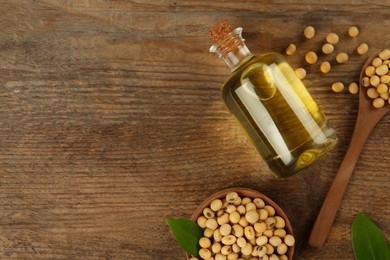 Photo of Glass bottle of oil, leaves and soybeans on wooden table, flat lay. Space for text