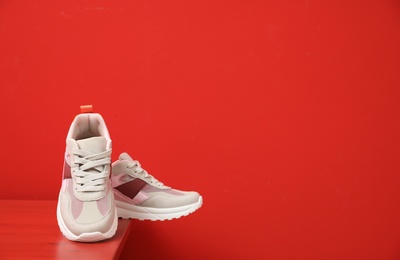 Photo of Stylish women's sneakers on wooden table near red wall, space for text