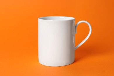Photo of One white ceramic mug on orange background