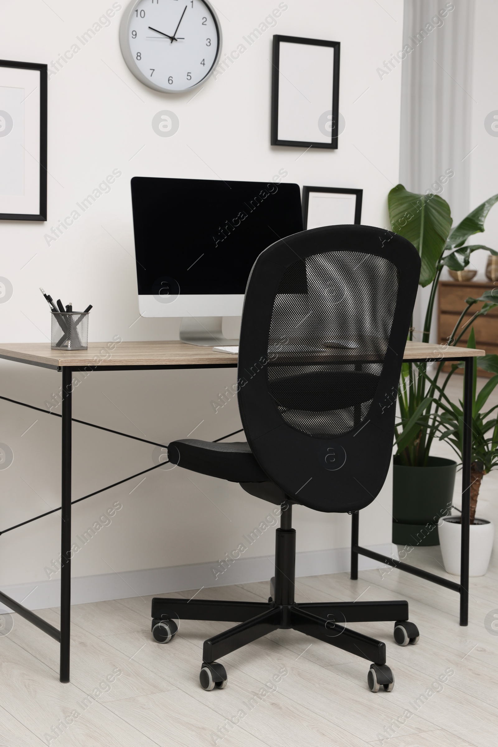 Photo of Comfortable office chair near desk and houseplants in modern workplace