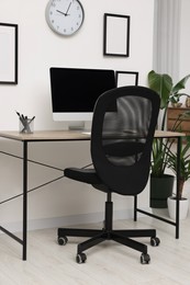 Photo of Comfortable office chair near desk and houseplants in modern workplace